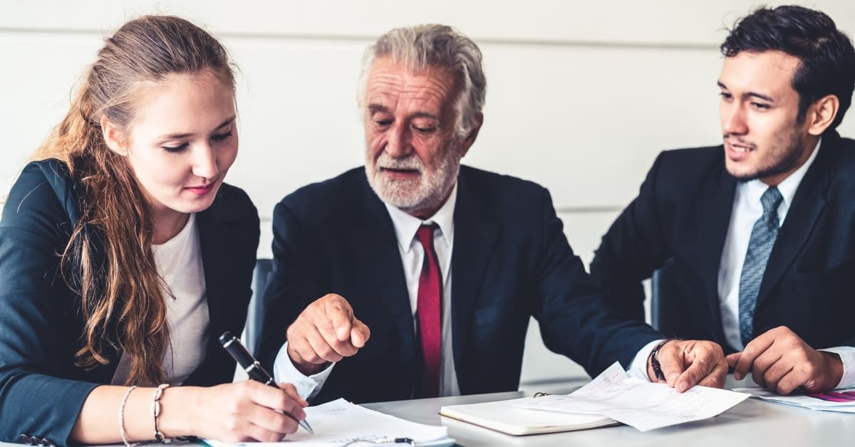 older financial planner with young couple signing papers