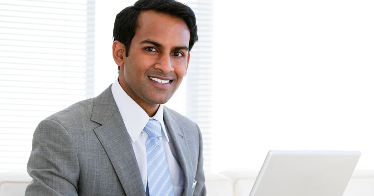 Man in Suit and Tie on Laptop Smiling for Camera