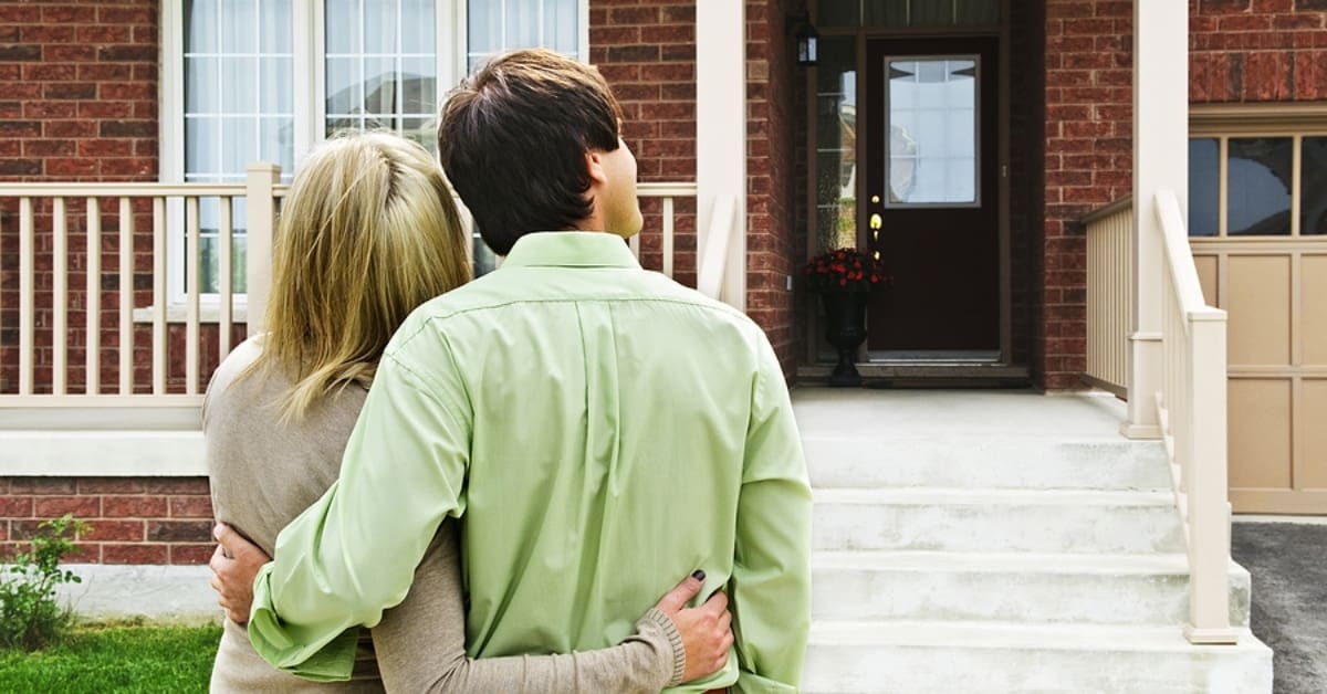 Couple Posing with Arms Around Each other Looking at their House