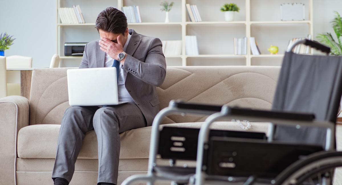Man sitting on couch looking upset with wheelchair next to him