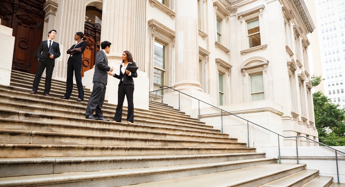 four well-dressed professionals standing on courthouse steps