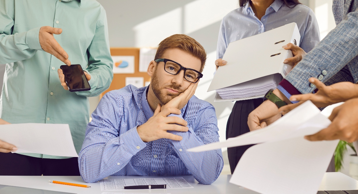 adult male sitting at desk looking frustrated while surrounded by files and documents