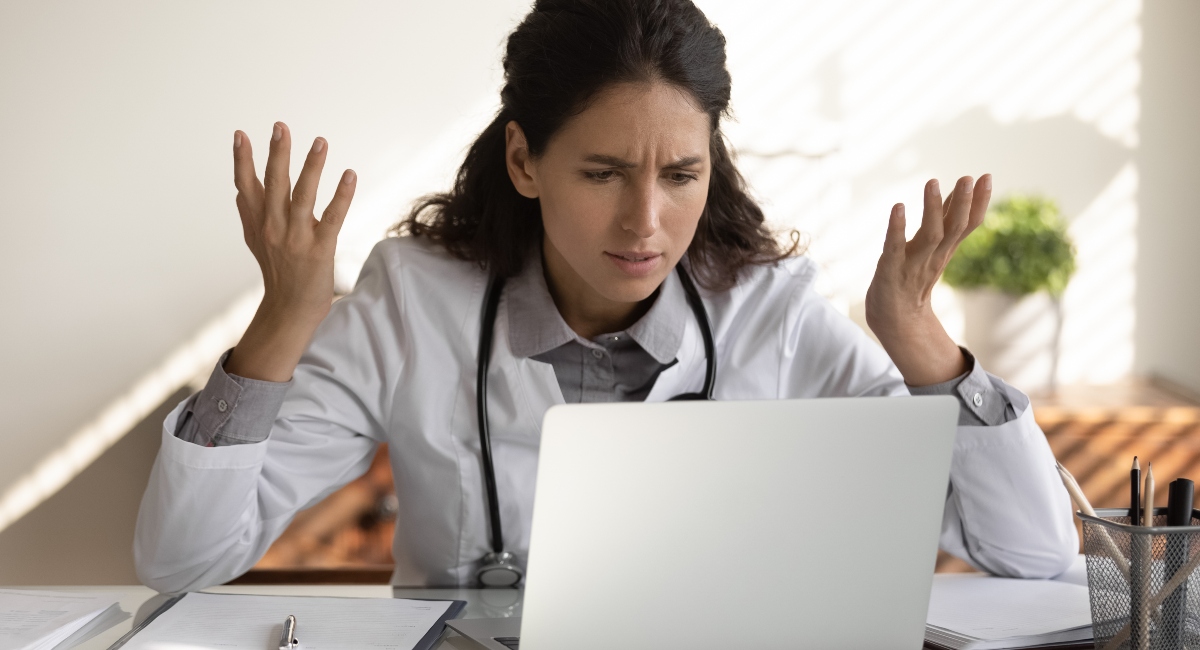 Angry female nurse work on laptop in clinic frustrated by student loan payments