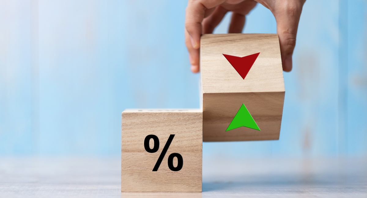 A man's hand holding a wood cube block with percentage sign and up/down arrow symbol on it