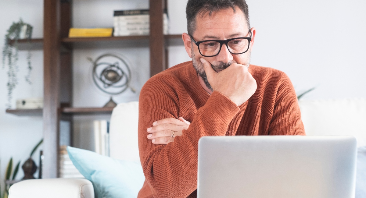 Frustrated man feeling tired and worried about student loan repayment sitting on sofa at home with laptop