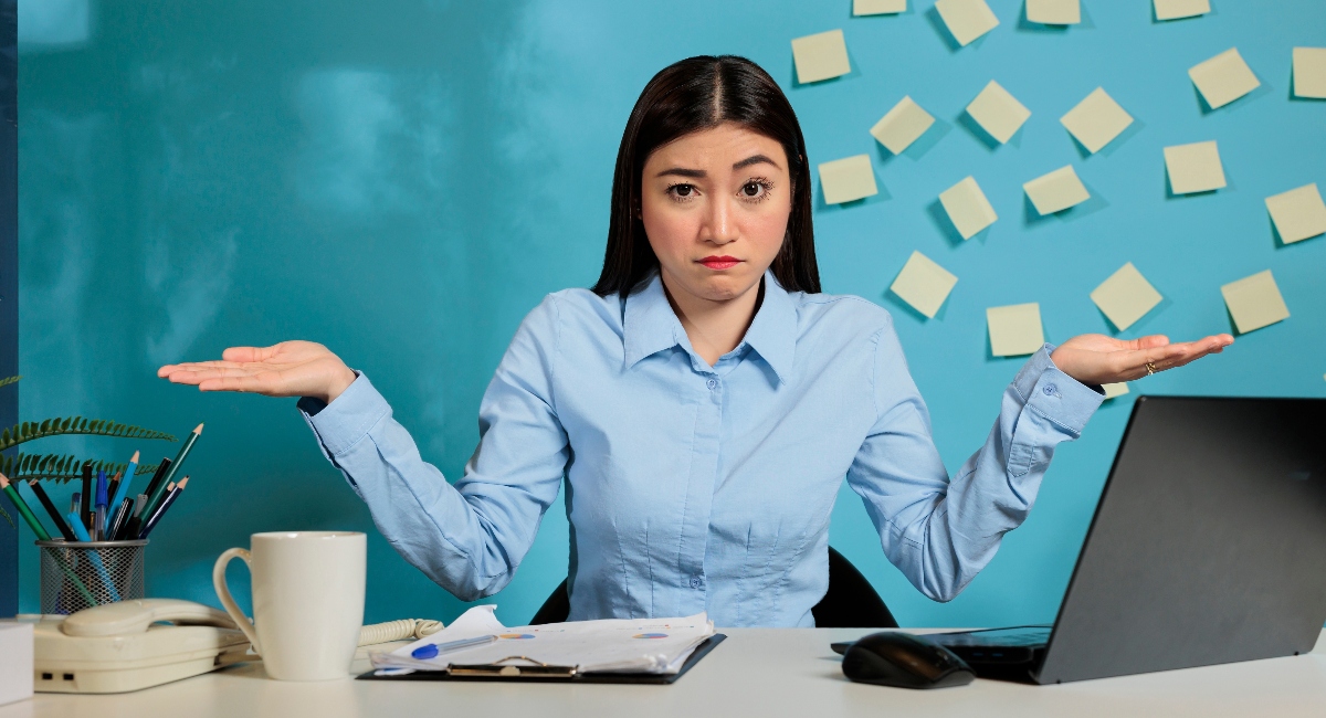 woman wearing blue shirt sitting at desk shrugging her shoulders