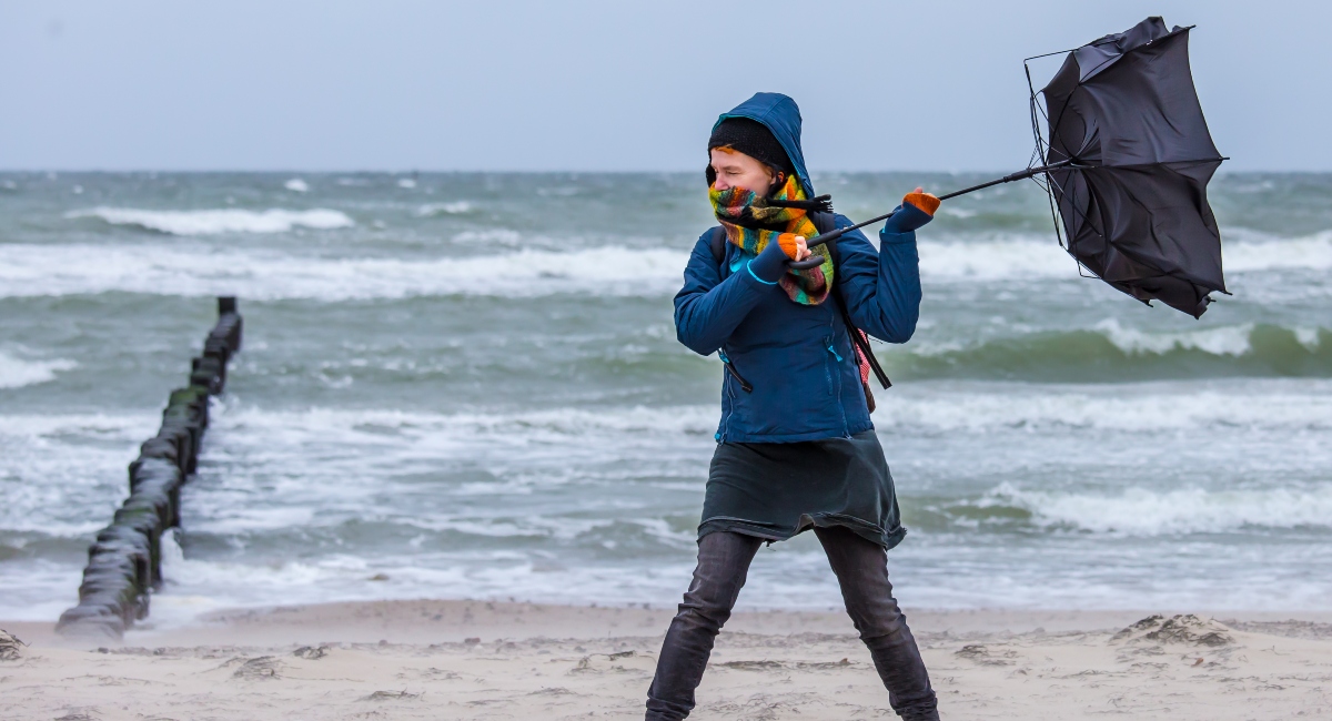 strong wind destroys a woman's umbrella during a beach walk