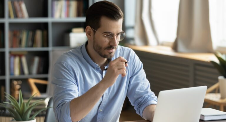 Concentrated young businessman in eyewear looking at laptop screen