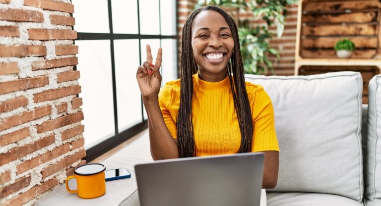 African woman sitting on the sofa using laptop at home smiling