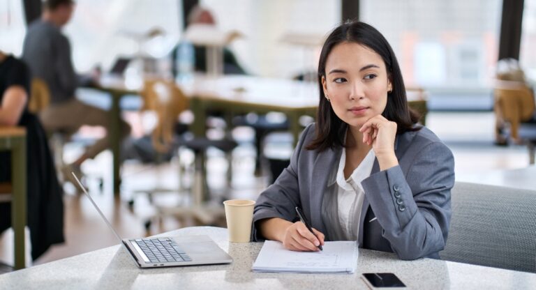 Young thoughtful Asian business woman executive sitting at a table with a laptop