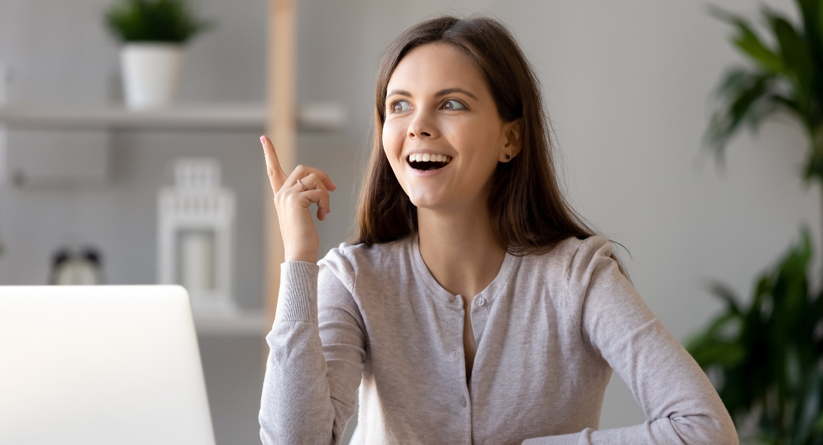 Young happy woman sitting at desk near laptop gesturing with hand to signal good idea