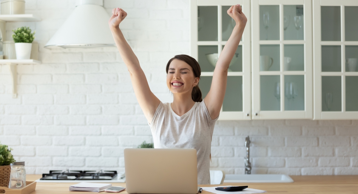 Woman and laptop, with hands in the air for success.